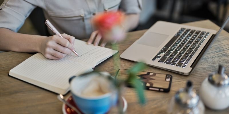 Woman writing on a notepad with laptop on table