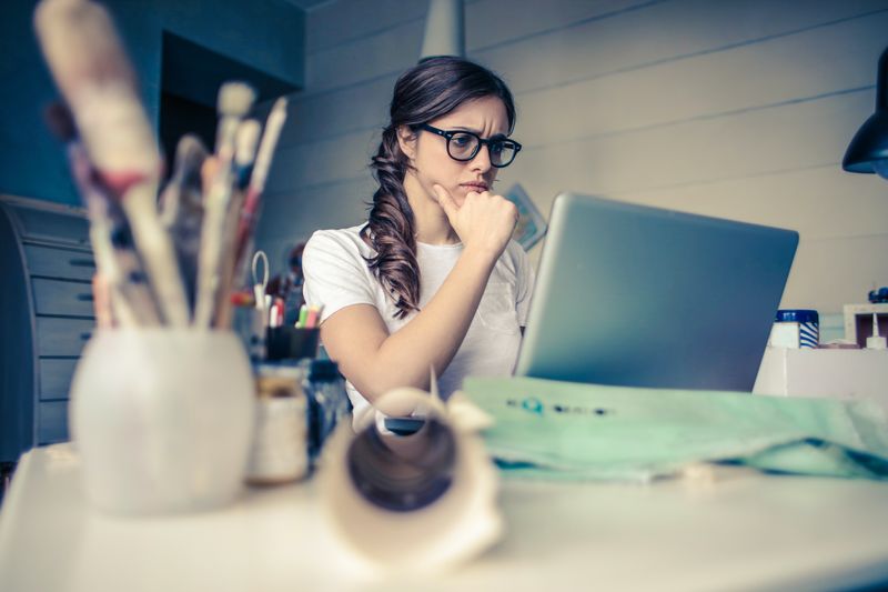 Brown haired woman thinking in front of a laptop