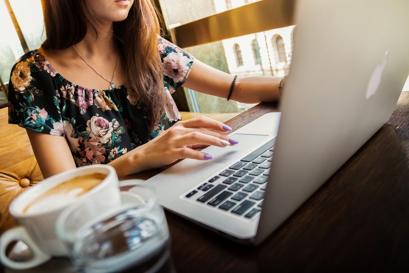 Lady in a black shirt sitting in front of a laptop with a coffee cup on the table